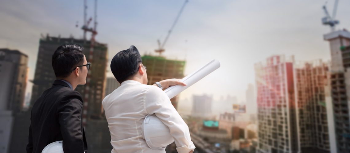 Asian businessman discuss with engineer architect in suite, looking and point to finger forward away and holding construction roll plan for working team concept, back view